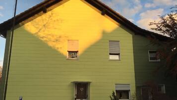 A two-story building with a green facade, a small front porch, and a visible garage door.