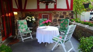 An outdoor patio with a stone wall, a red and white painted ceiling, and two green floral chairs around a white table with a flower centerpiece. - in Bernsfeld mit großem Garten by Interhome (Atzenhain)