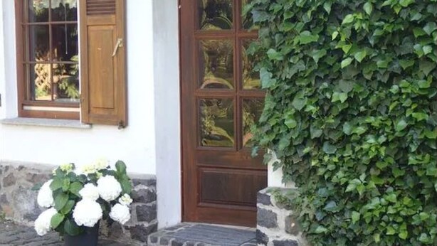 A building with a wooden door and windows, a stone step, and a potted plant with white flowers. - in Bernsfeld mit großem Garten by Interhome (Atzenhain)