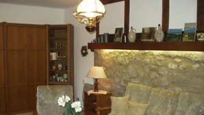 A cozy living room with a stone wall, a wooden cabinet, a sofa, and a table with a vase of flowers. - in Bernsfeld mit großem Garten by Interhome (Atzenhain)