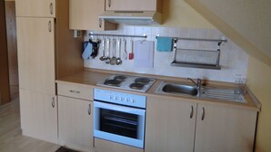 Una cucina compatta con fornello, forno e lavandino, caratterizzata da mobili in legno e un porta utensili a parete.
