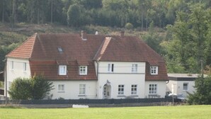 Een huis met twee verdiepingen, voorzien van een rode tegelsdak, witte muren en een klein voortuintje.