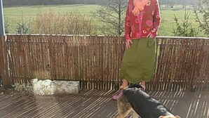 Een persoon staat op een houten terras met een hond.