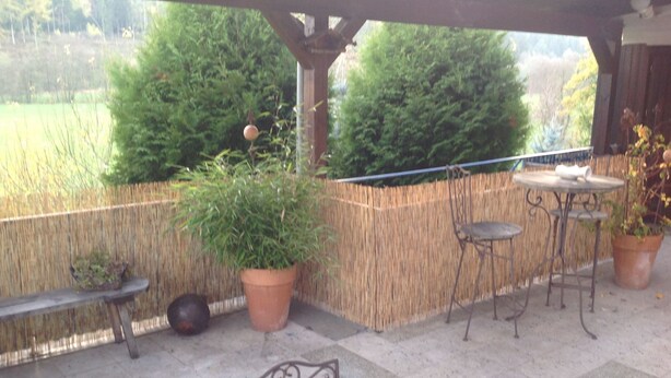 Een terras buiten met een tafel en stoelen, een bankje en potplanten.