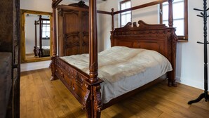 A four-poster bed with a wooden frame and a white bedspread in a room with wooden floors and a large mirror on the wall. - in Traben mit Kleinem Garten by Interhome (Traben-Trarbach)