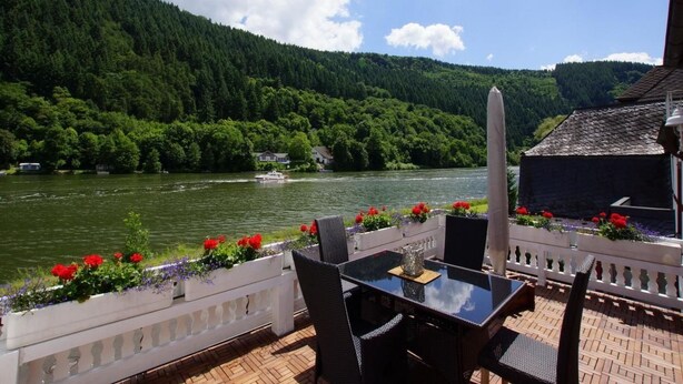 Ein Sitzbereich im Freien mit Tisch und Stühlen mit Blick auf einen Fluss und bewaldete Hügel.