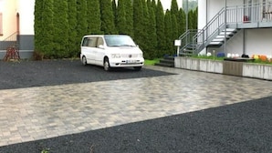 En hvid varevogn parkeret i en indkørsel med belagt areal og en trappe til en bygning.