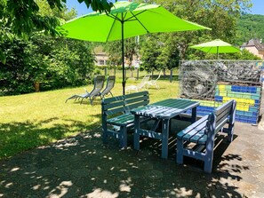 A patio area with a table and chairs, surrounded by greenery and a view of a hill. - Lollipop by Interhome (Alf)