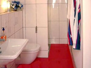 A bathroom with a white bathtub, a toilet, and a red floor. - Lollipop by Interhome (Alf)