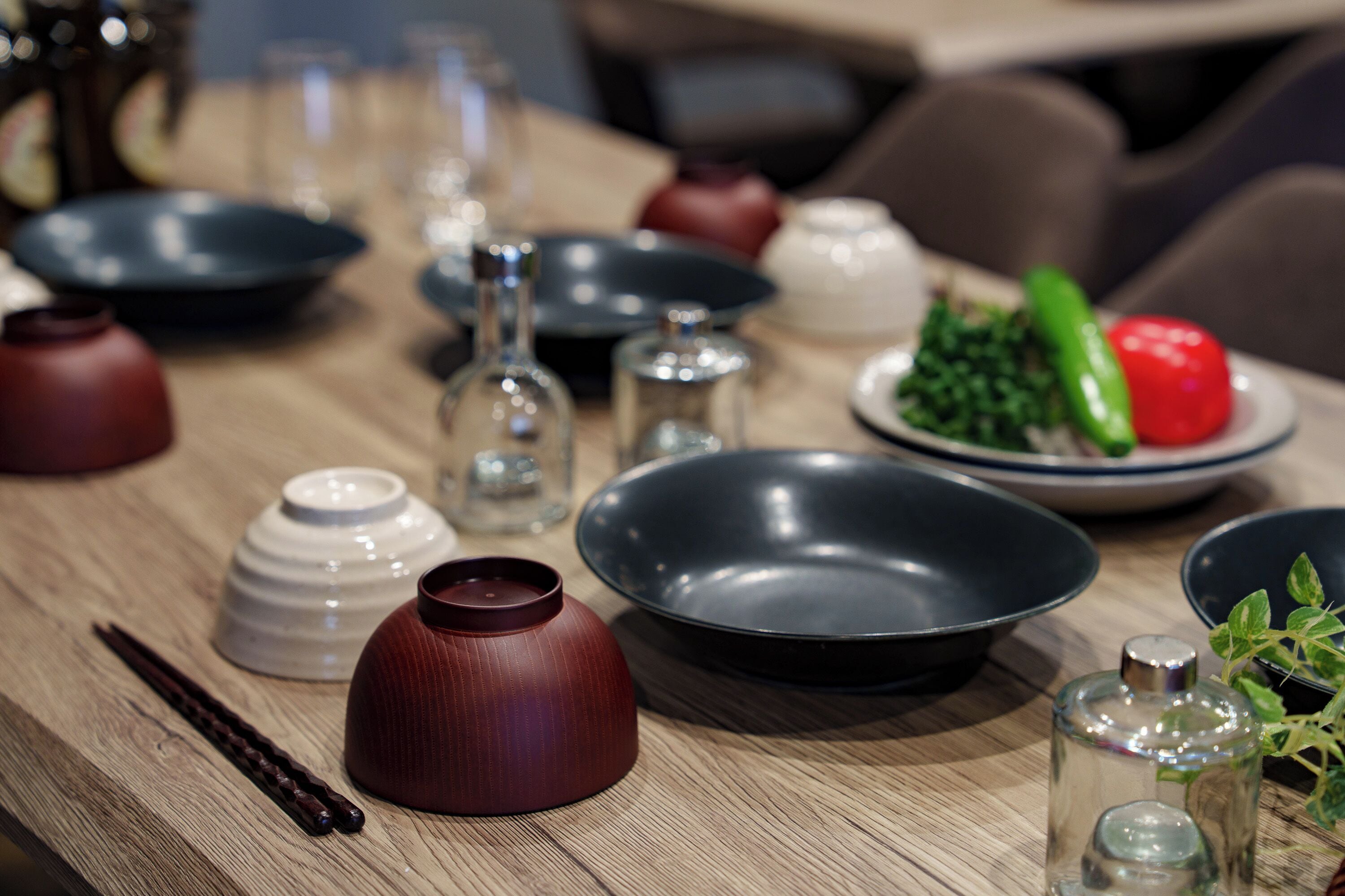 Una mesa de comedor con varios platos, un florero rojo, palillos y un pequeño recipiente de vidrio.