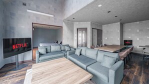 A modern living room with a sectional sofa, a wooden coffee table, and a flat-screen TV displaying the Netflix logo. - PROSTIMO (Bibai)