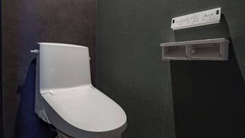 Moderni kylpyhuone, jossa on valkoinen wc-istuin, seinälle asennettu huuhtelusäiliö ja pieni hylly, jossa on ohjauspaneeli.