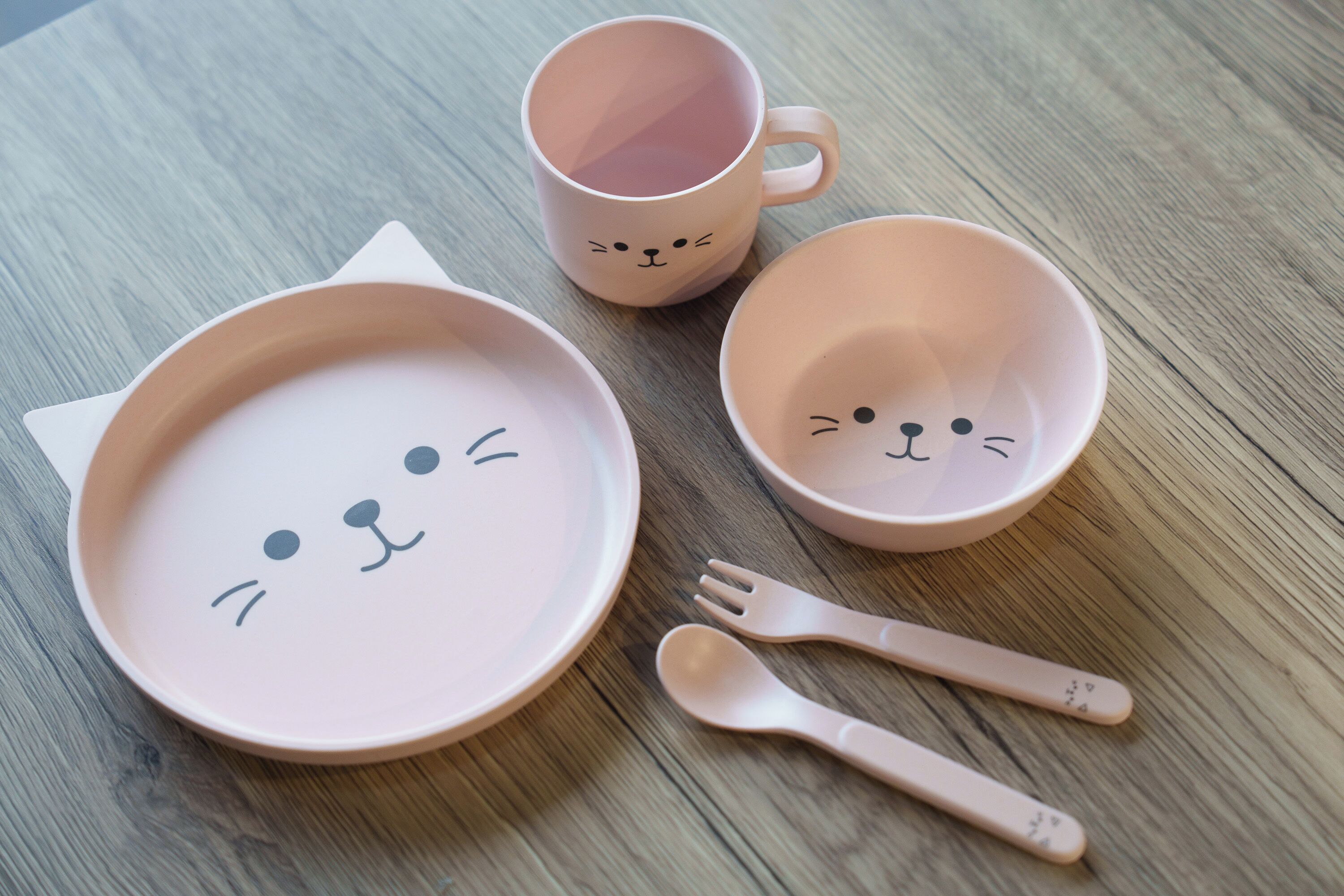 A table with a pink ceramic plate, a pink ceramic cup, a pink ceramic bowl, and a pink fork.