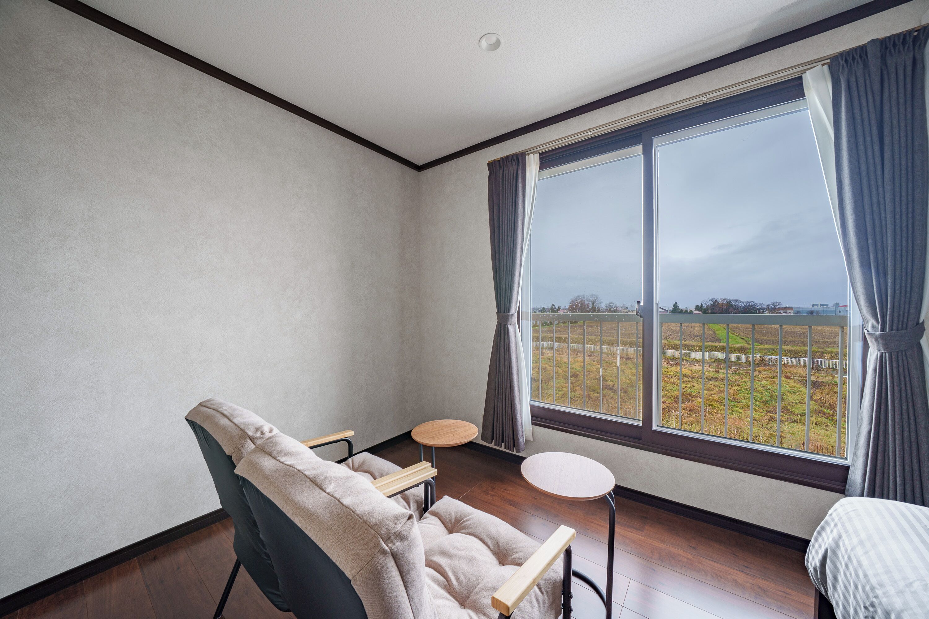 A room with a large window, a chair, a small round table, and a bed.
