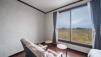 A room with a large window, a chair, a small round table, and a bed.