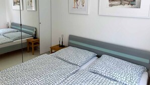Une chambre d’hôtel avec deux lits, une table de chevet, un miroir et des œuvres d’art accrochées aux murs.