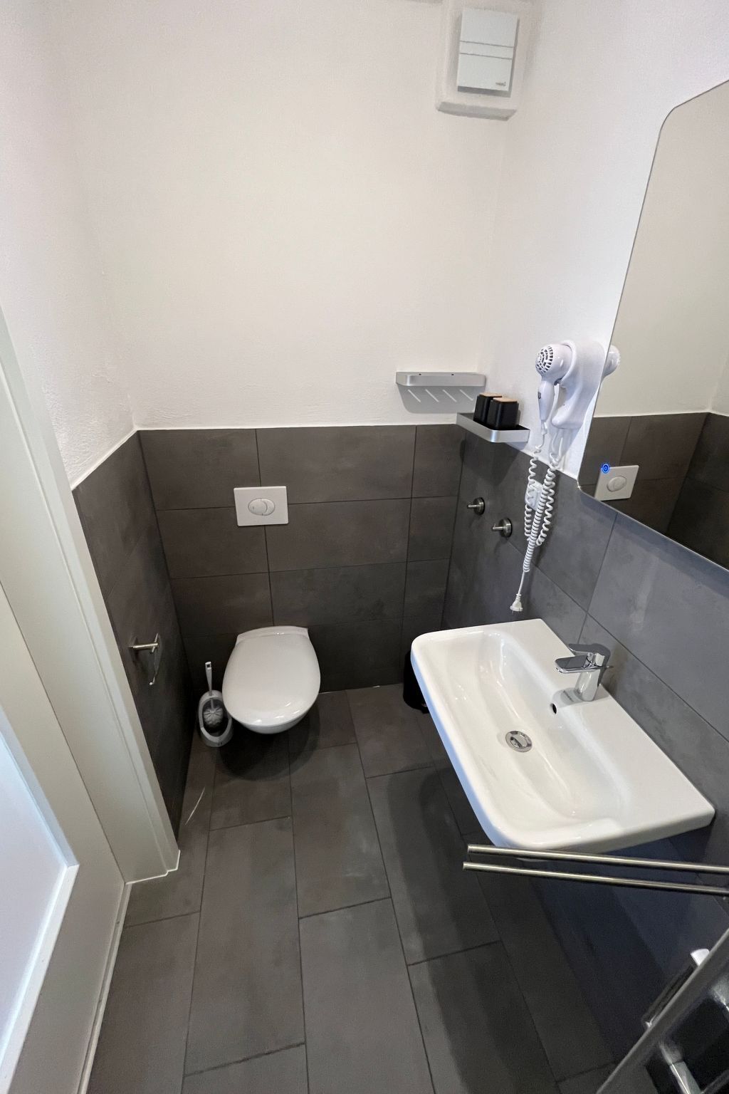 A compact bathroom with a toilet, a sink, and a hand dryer.