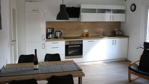 A modern kitchen with white cabinets, a wooden countertop, a black pendant light, and a dining area with a table and chairs. - Haus Budinger by Interhome (Alf)