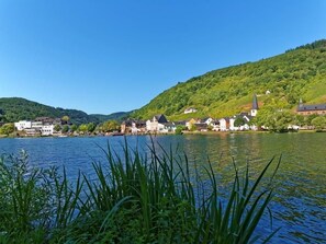 Une ville riveraine, avec des bâtiments qui bordent le cours d’eau, une église et des collines en arrière-plan.