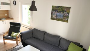 A modern living room with a grey sofa, a white coffee table, a wooden chair with a green cushion, and a pendant light. - Haus Budinger by Interhome (Alf)