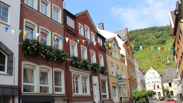 A row of traditional European townhouses with a clear street view, a red car parked on the side, and a hillside in the background. - Haus Budinger by Interhome (Alf)