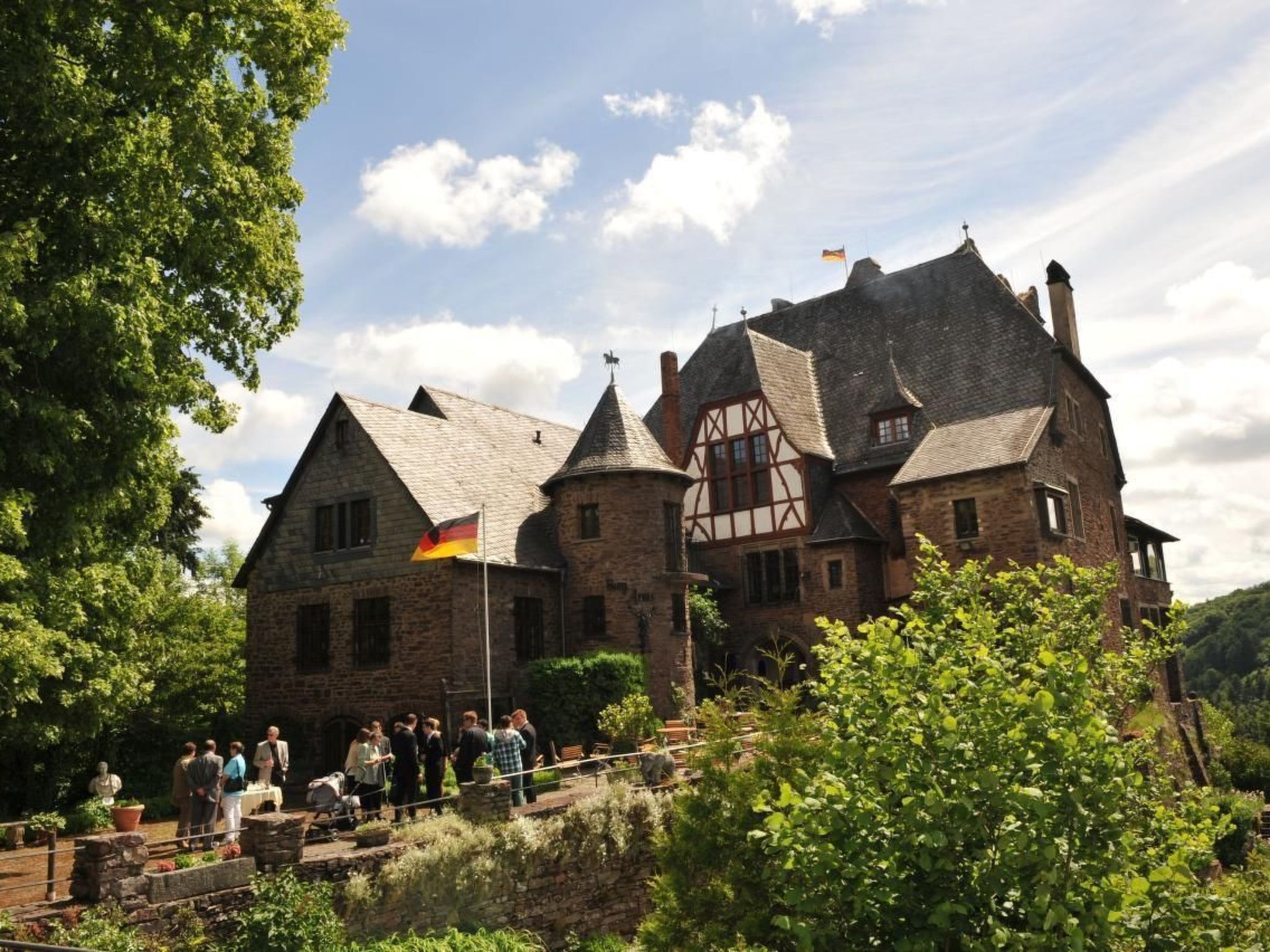 A historic stone building with a prominent tower, surrounded by lush greenery and a clear sky.