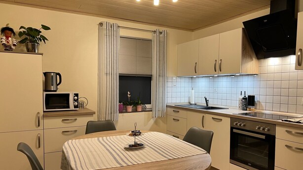 A modern kitchen with a round dining table, built-in oven, and a microwave. - Apartment Im Hof by Interhome (Pittenbach)