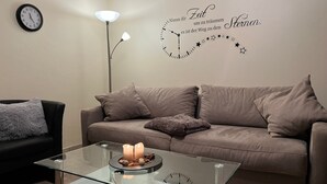 A living room with a glass coffee table, a sofa, a black armchair, a wall clock, and a decorative wall with text and stars. - Apartment Im Hof by Interhome (Pittenbach)