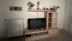A modern living room with a flat-screen TV on a wooden entertainment unit, a radiator, and several potted plants on shelves. - Apartment Im Hof by Interhome (Pittenbach)