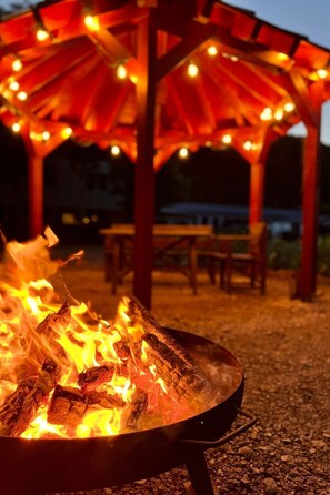 Un braciere con legna ardente, circondato da una pergola rossa con luci a catena.