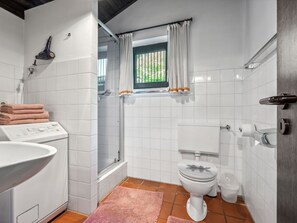 Ein Badezimmer mit weißen Fliesen, einer Dusche, einer Toilette, einem Waschbecken und einem Fenster mit Vorhängen.