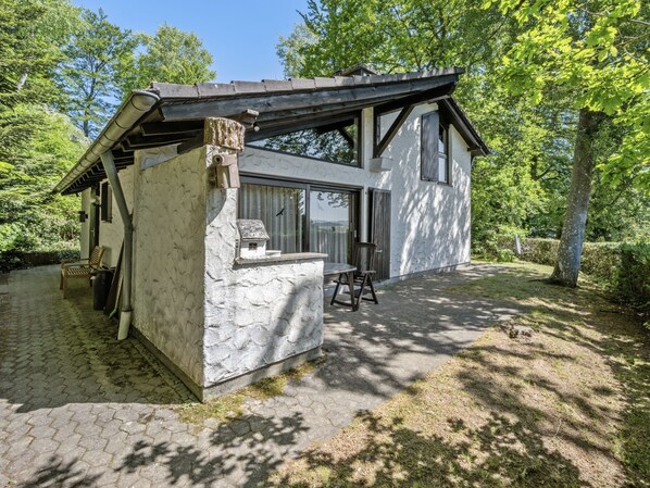 Ein modernes Haus mit Natursteinfassade, einer Holzterrasse und einem großen Fenster.