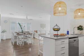 A modern kitchen with white cabinetry, a central island, and pendant lighting. - Sanctuary Splash Getaway (Sanctuary Point)