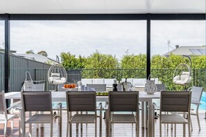 Un patio exterior con piscina, mobiliario blanco y sillones colgantes.
