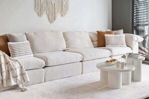A modern living room with a sofa, a coffee table, and a macrame wall hanging.