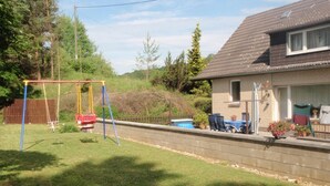 Un patio trasero residencial con un columpio, una zona de barbacoa y una piscina pequeña.