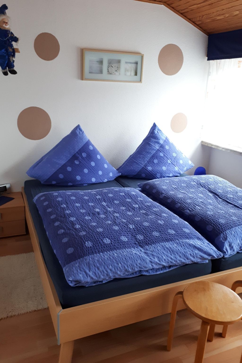 Una cama con ropa de cama y almohadas azules, un cabecero de madera y un pequeño taburete de madera.
