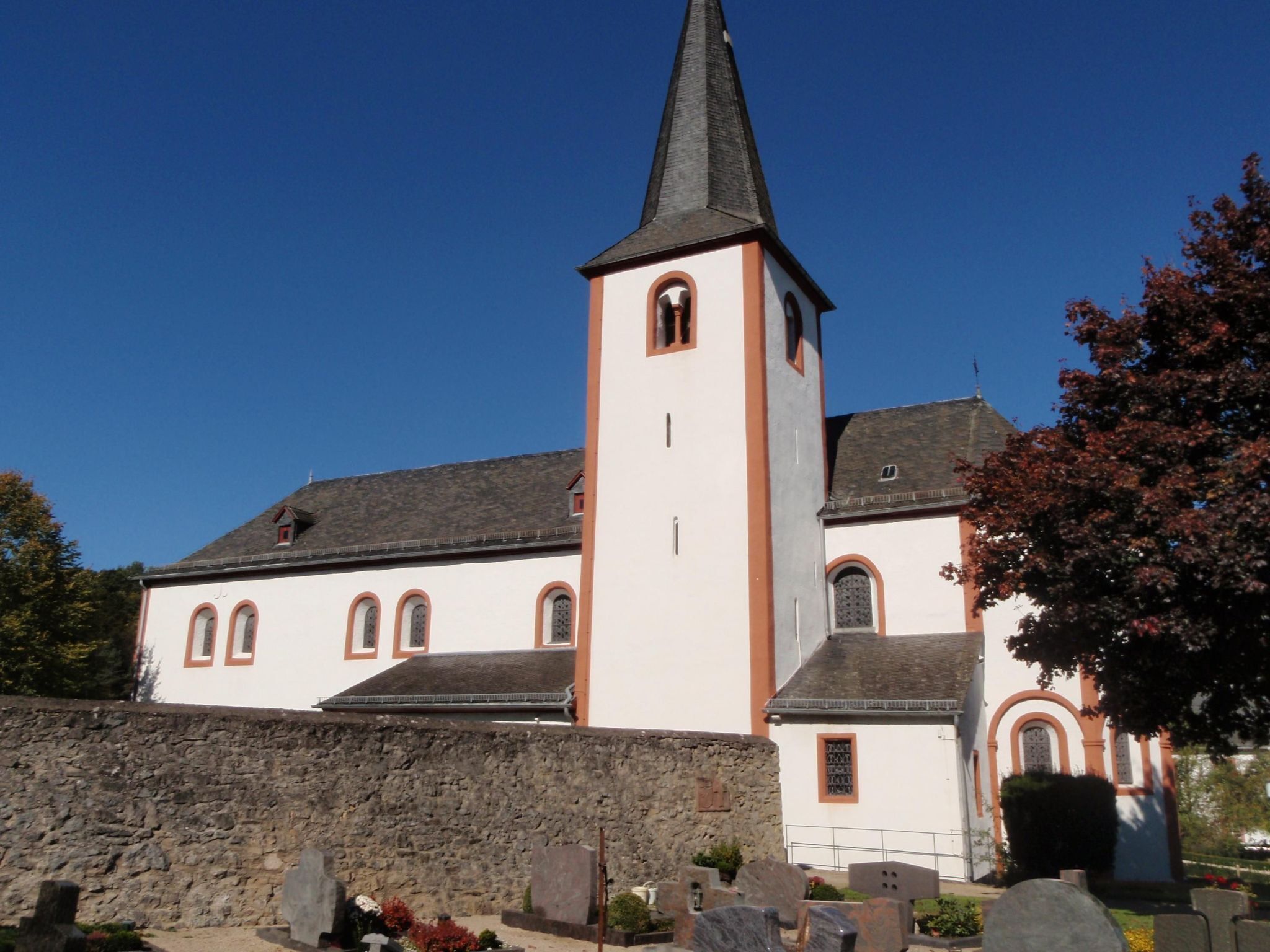 A church with a tall steeple and a stone wall in front.