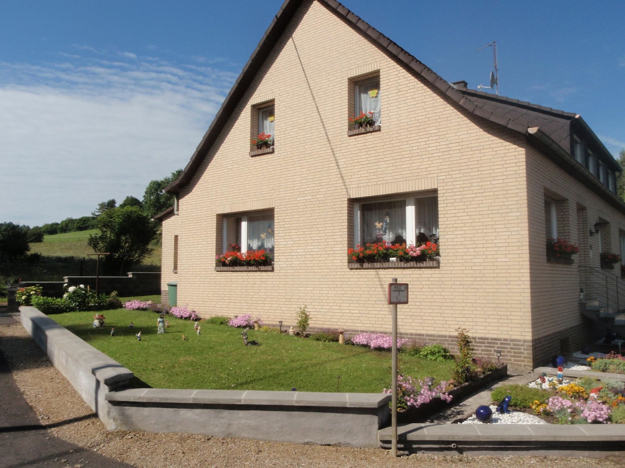 A two-story building with a sloped roof, rectangular windows with flower boxes, and a small garden area with various plants and flowers.