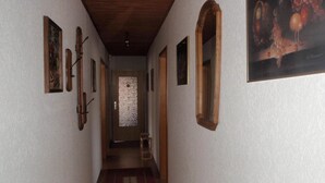 Un estrecho pasillo con vigas de madera en el techo, una puerta con panel de vidrio satinado y cuadros enmarcados en las paredes.