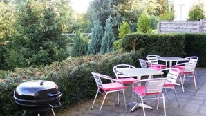 An outdoor patio with a grill, white metal chairs with pink cushions, and a hedge in the background. - Haus Sonnenhang by Interhome (Esch)