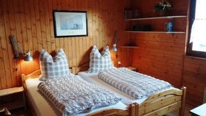 A wooden-paneled room with two single beds, a framed picture on the wall, and a shelf with books and a plant. - Haus Sonnenhang by Interhome (Esch)