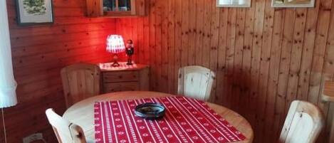 A wooden dining room with a round table, red and white checkered chairs, and wall-mounted light fixtures.