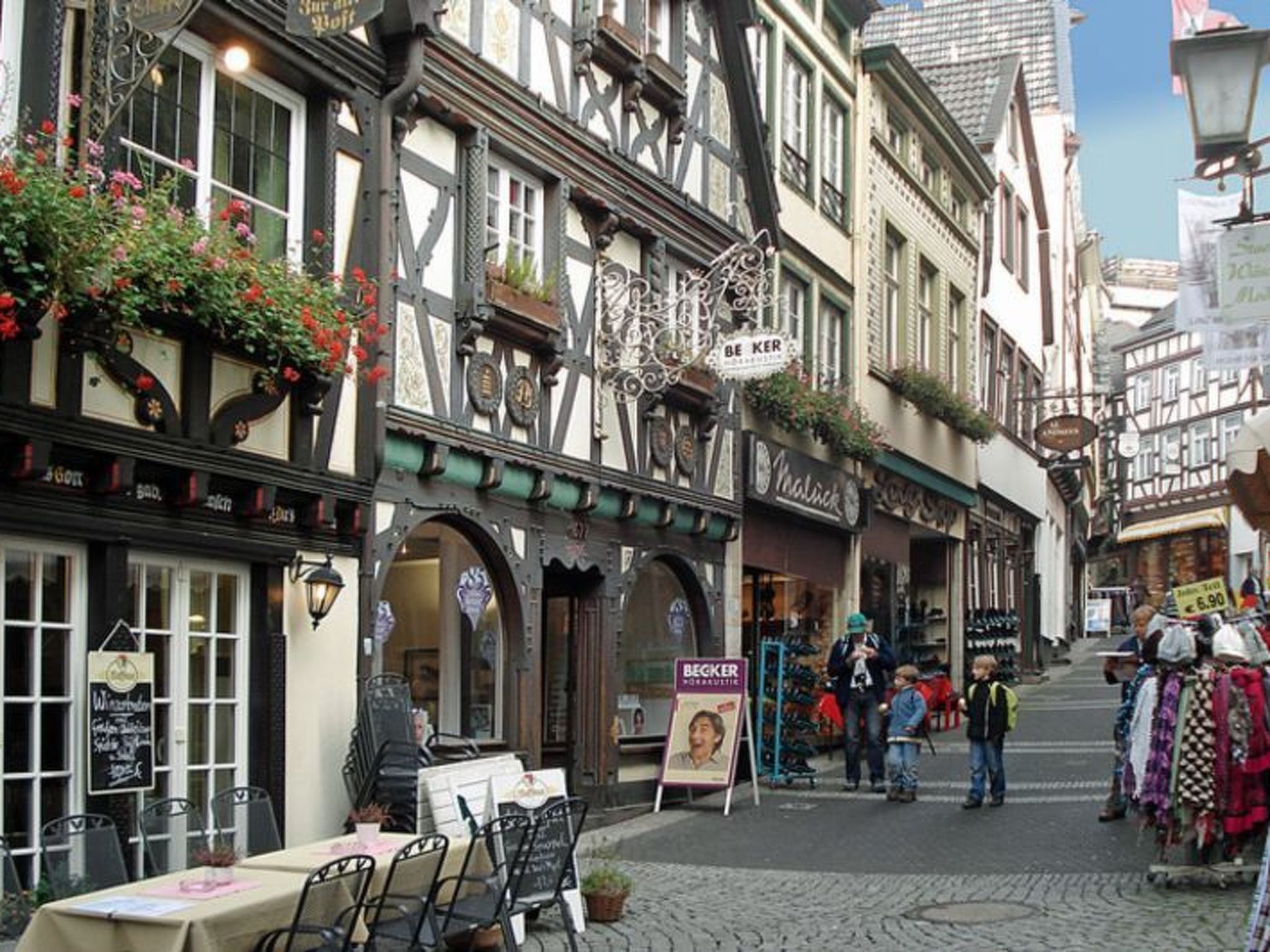 Eine typische europäische Straße mit Fachwerkhäusern, Außenbestuhlung und einem Marktstand.