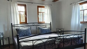 Une chambre à coucher avec un cadre de lit en métal, un plancher en bois, deux fenêtres avec des rideaux et une poutre en bois au plafond.