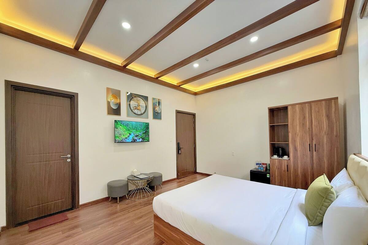 A modern bedroom with a large bed, wooden flooring, a TV, and built-in wooden shelving.