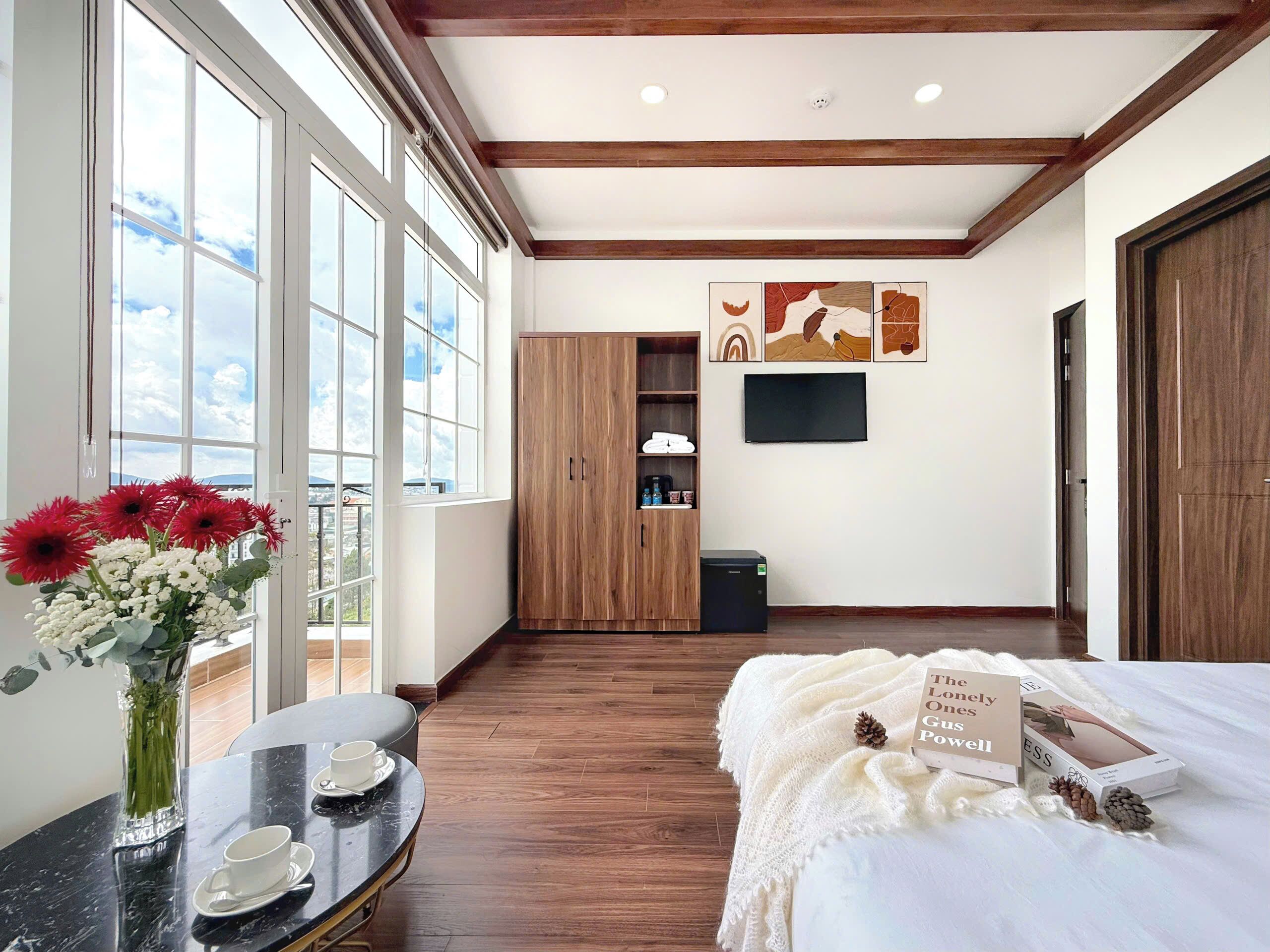 A hotel room with a large window, a wooden wardrobe, a flat-screen TV, and a cozy bed area with a sign reading "The Lonely Guy's Poverlo".