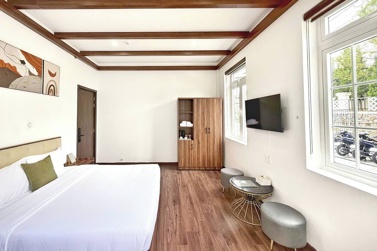 A bedroom with a bed, wooden wardrobe, TV, and a window with a view of parked motorcycles.