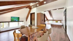 A spacious room with a wooden dining table and chairs, a television, and a loft bedroom with a bed. - KIEN DALAT (Lam Vien - Da Lat)