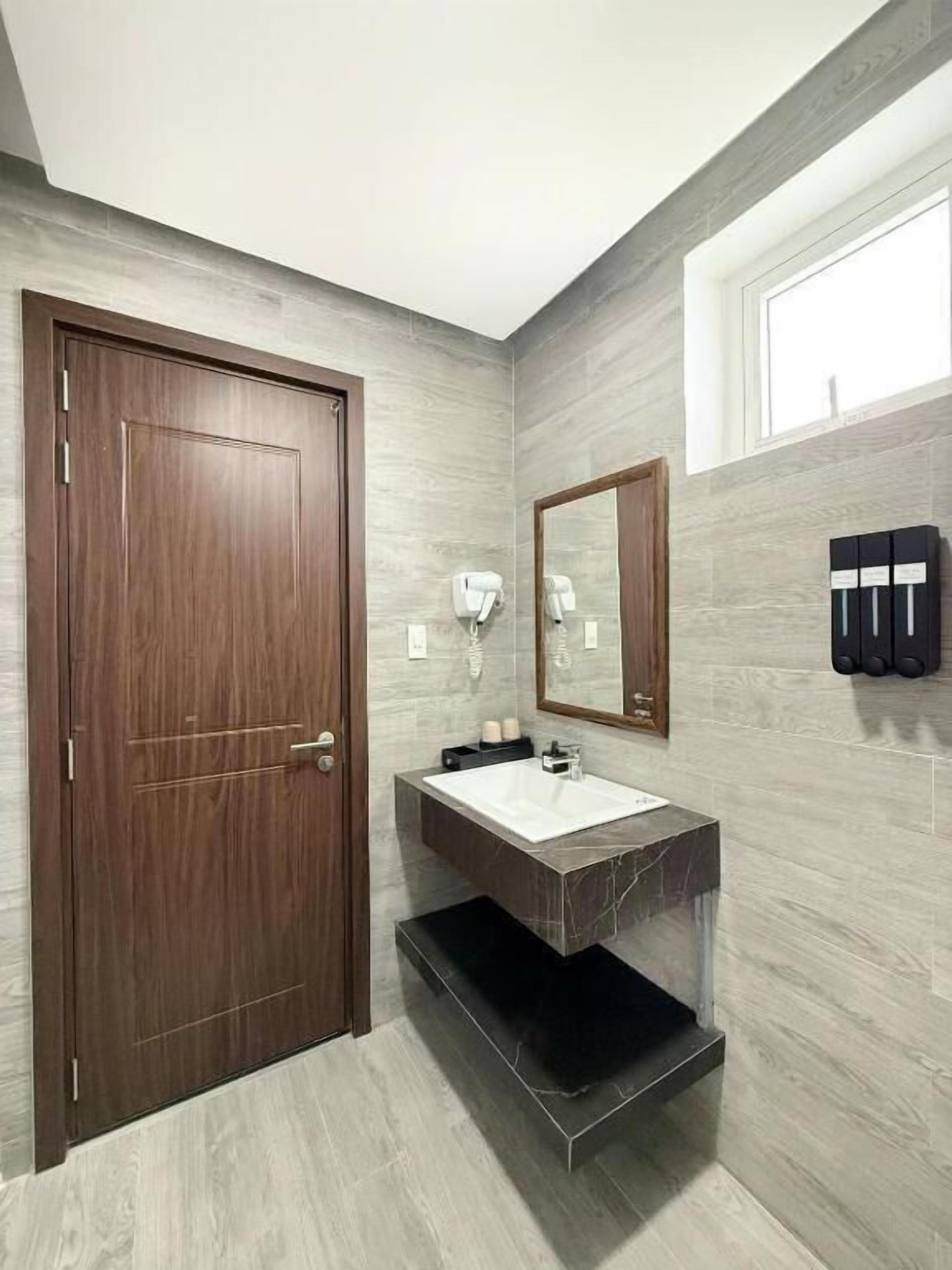 A modern bathroom with a wooden door, a marble sink, a mirror, and a window.